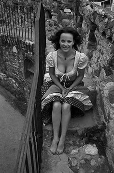 a woman is sitting on the steps in front of some stone walls and stairs, smiling at the camera