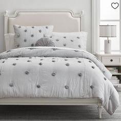 a bed with white linens and silver decorations on the headboard, along with two nightstands