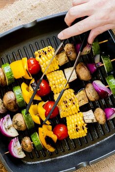 a person is cutting up vegetables on a bbq grill with two large tongs