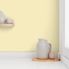 two white vases are sitting on a shelf in front of a yellow painted wall