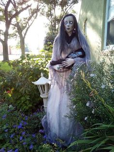 a creepy doll is standing in the middle of some flowers and bushes with her hands on her chest