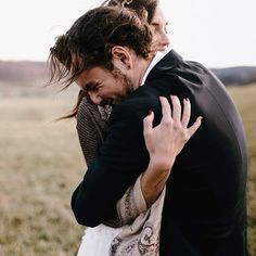 a man and woman hugging in the middle of a field