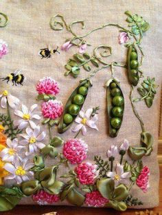 an embroidered pillow with flowers, peas and other things on it sitting on a table