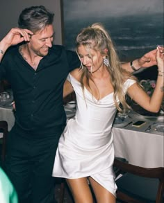 a man and woman dancing together at a dinner table with wine glasses on the table