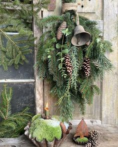 a wreath with pine cones and evergreens hanging from the front door, next to a candle