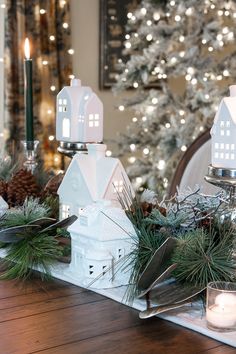 a table topped with white christmas decorations and candles next to a tree covered in lights