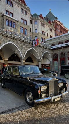 an old black car is parked in front of a large building with arched doorways