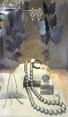 an assortment of jewelry is displayed in a glass case with butterflies on the wall behind it