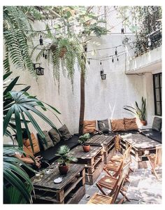 an outdoor seating area with wooden tables and chairs, surrounded by greenery on the patio