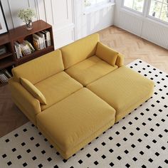 a yellow couch sitting on top of a white rug in front of a book shelf