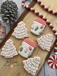 decorated christmas cookies on a wooden board next to candy canes and pine cone decorations