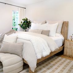 a bed with white sheets and pillows in a bedroom next to a window filled with plants