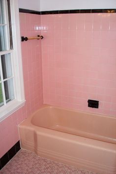 a bathroom with pink walls and black trim on the tub, window, and tile floor