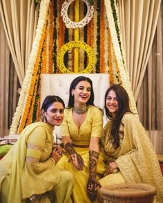 three beautiful women sitting next to each other in front of a decorated stage with flowers