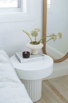 a white table with a book and candle on it in front of a large mirror