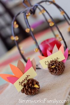 two paper turkeys are sitting on a table with pine cones and place cards in front of them