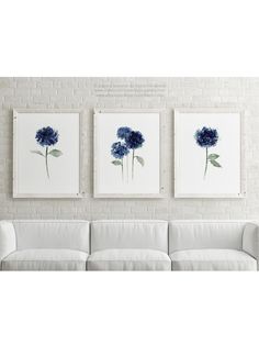 three blue flowers are hanging on the wall above a white couch in front of a brick wall