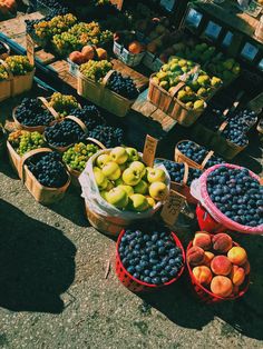 several baskets of fruit sitting on the ground in front of some boxes with apples and blueberries