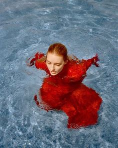 a woman floating in the water wearing a red dress