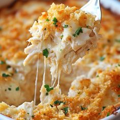 a spoonful of cheesy chicken casserole is being lifted from the casserole dish