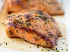 two pieces of meat sitting on top of a cutting board covered in herbs and seasoning