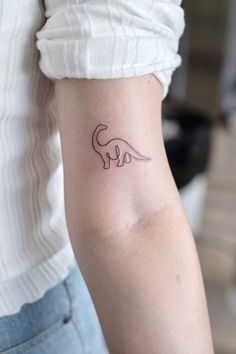 a woman's arm with a small dinosaur tattoo on the left side of her arm