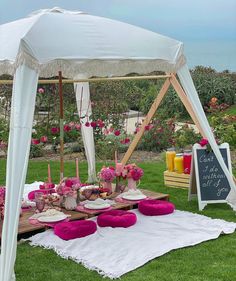 a table with pink pillows under a white tent on the grass near flowers and plants