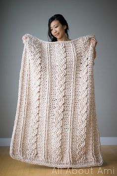 a woman is holding up a crocheted blanket