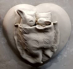 a white heart shaped sculpture with two rabbits in it's pouch on a table