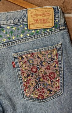 the back pocket of a pair of jeans with flowers and crosses on it, sitting on a wooden floor