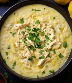 a bowl filled with soup and garnished with parsley on the table next to lemons