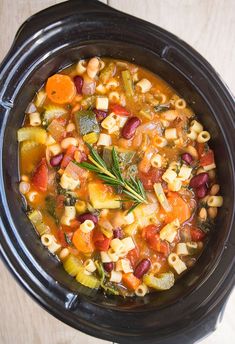 a black crock pot filled with soup and vegetables on top of a wooden table