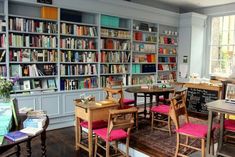 the library is full of books and many tables with chairs around them in front of large windows