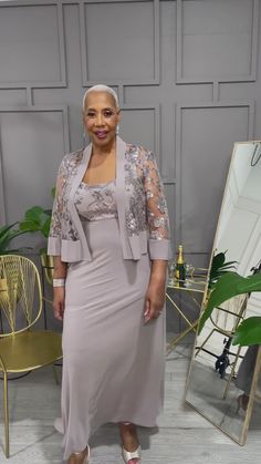 a woman standing in front of a mirror wearing a dress and jacket with lace sleeves