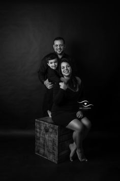 a man and woman pose for a black and white photo with their son in front of a dark background