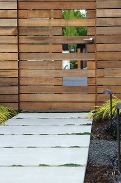 a wooden fence with grass growing on the ground and in front of it is a white walkway