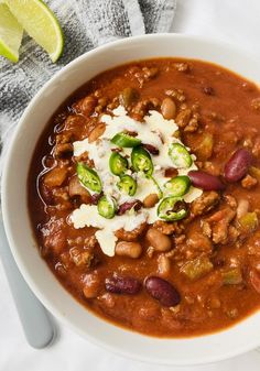 a white bowl filled with chili, beans and cheese next to a lime slice on the side