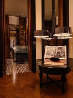 an open book sitting on top of a wooden table next to a lamp and mirror