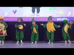 several children in green and yellow outfits on stage with their hands out to the side