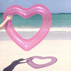 a heart shaped balloon being held by a woman on the beach