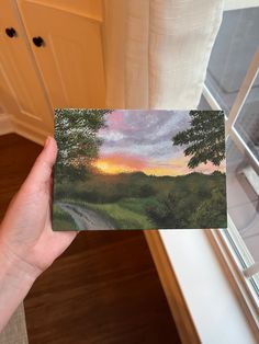 a person holding up a card with a painting on it in front of a window