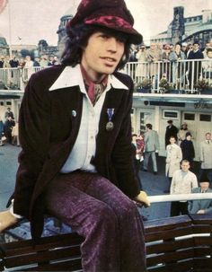 a man sitting on top of a bench wearing a hat and purple pants with people in the background