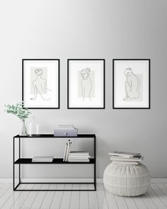 three framed pictures hang on the wall next to a table with books and a vase