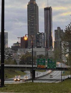 cars driving down the road in front of tall buildings and skyscrapers at dusk with traffic lights on