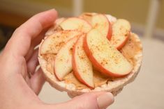 a person is holding up a small pastry with apples on top and cinnamon sprinkles