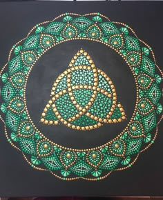 a painting with green and gold designs on black paper, in the shape of a circle