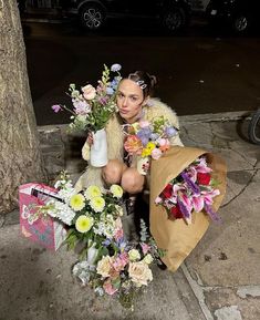 a woman is sitting on the sidewalk with flowers