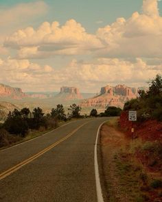 an empty road in the desert with mountains in the backgrouund and clouds in the sky