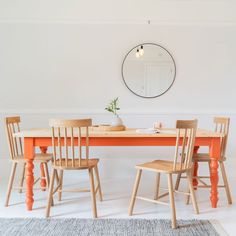 an orange table with four chairs and a mirror on the wall in a white room