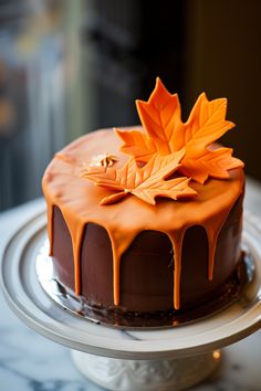 a chocolate cake with orange icing and maple leaf decoration on top, sitting on a plate